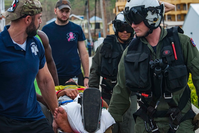 Men in uniform carry a person on a stretcher.