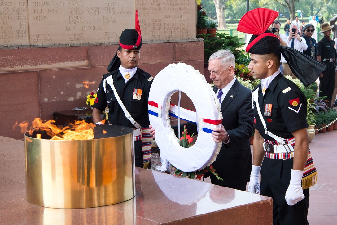 Defense Secretary Jim Mattis, flanked by two Indian service members, holds a wreath while standing before an eternal flame.