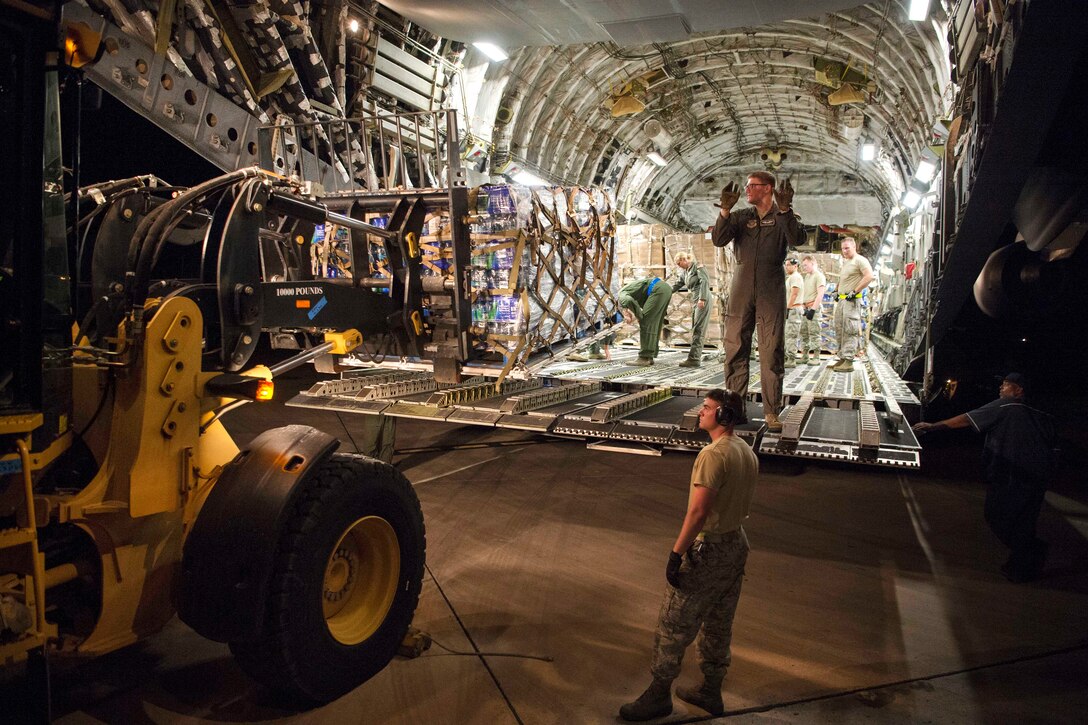 An airman directs a forklift operator to back up while off loading a pallet of water from a C-17 Globemaster III aircraft.