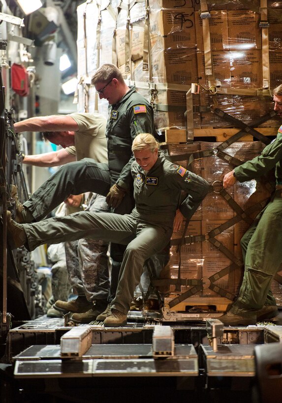 Maj. Kari Fleming, foreground, and other airmen push a pallet of food off from a C-17 Globemaster III aircraft.