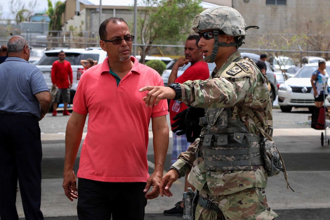 A soldiers points as he assists a person on the street.