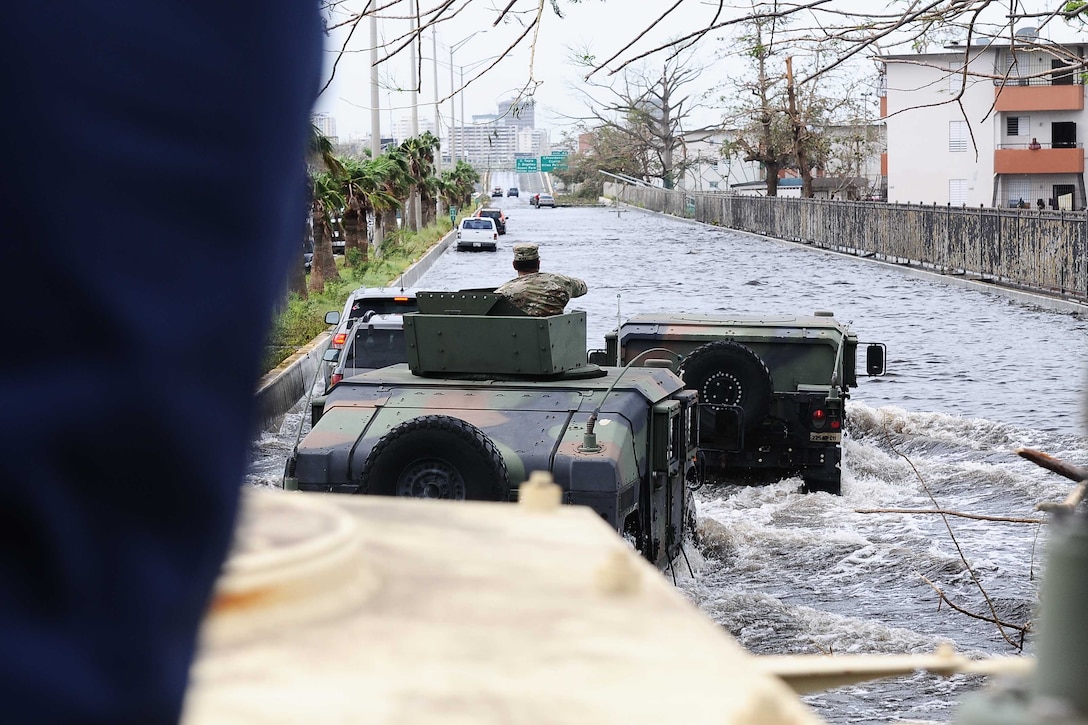 A soldier in a vehicles looks at a flooded highway.