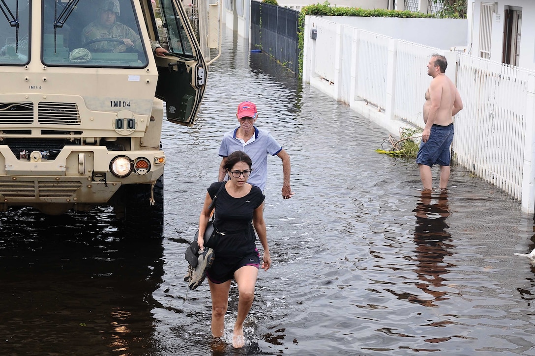 Three people wade through a flooded street.