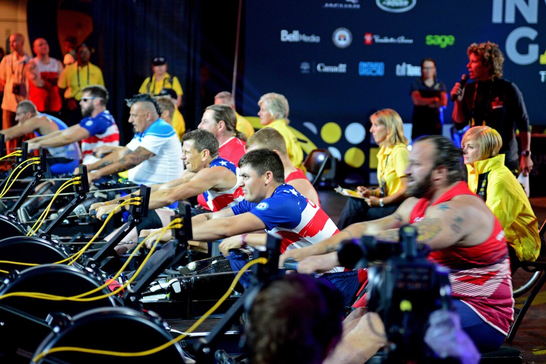 A line of athletes use rowing machines.