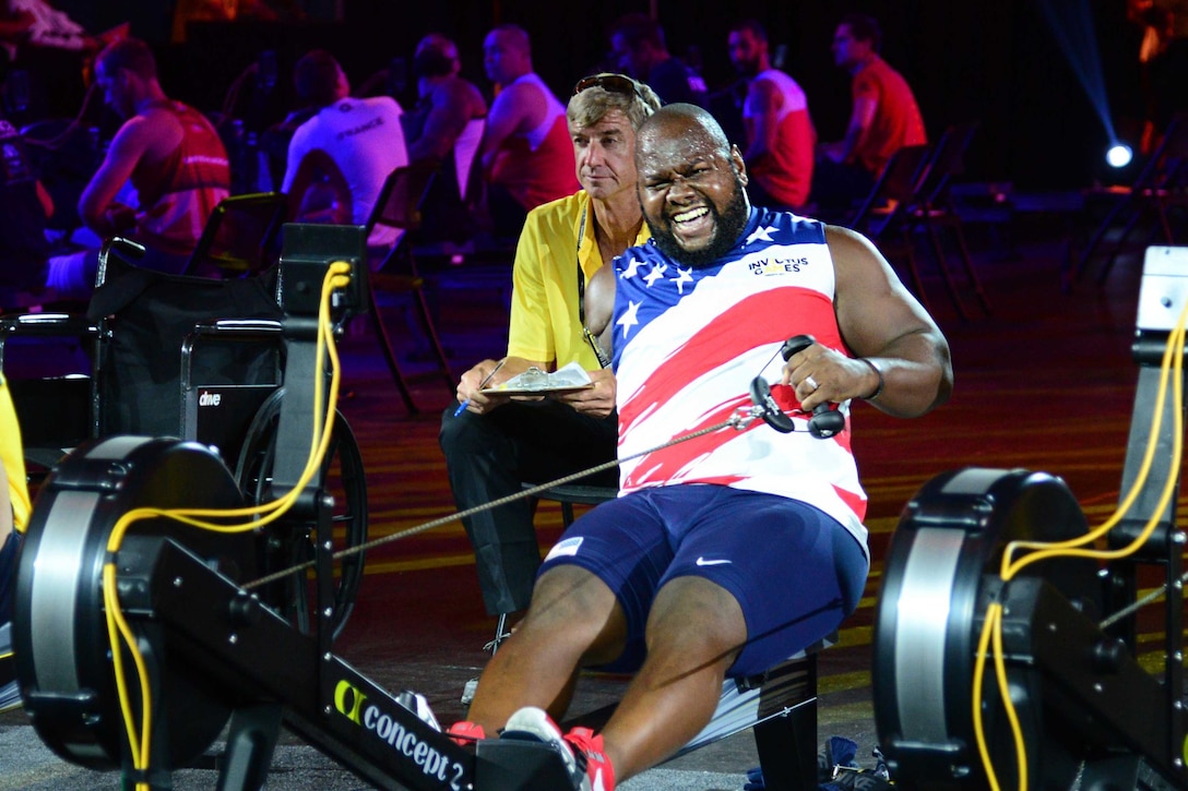 A person uses a rowing machine with another person sitting behind him.