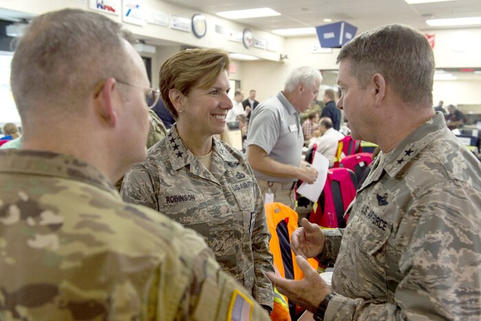 Military personnel speak in a crowded room.