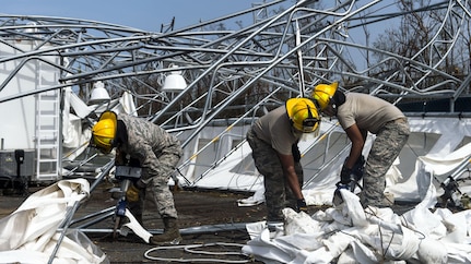 Troops in hard hats clean up debris on the ground near mangled metal structures.