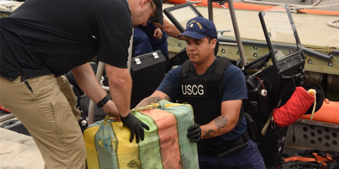 A  Coast Guard Cutter Valiant crew member passes a bale of cocaine to a drug enforcement agent during a drug offload at Station Fort Lauderdale, Sept. 26, 2017.