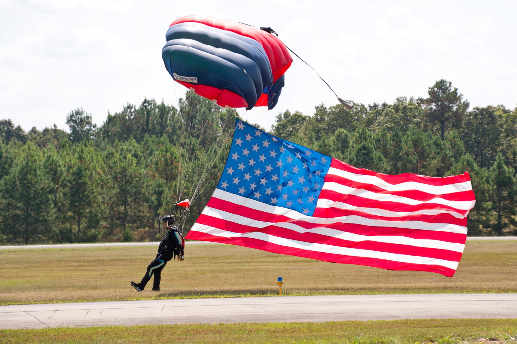 Craig Dumey, who is member of the Southeast Missouri Skydiving Club, parachutes into the drop zone with the American Flag during opening ceremonies at the “Wings Over The Rock Air Show and Car Show” at the North Little Rock Airport, in North Little Rock Airport, Ark., Sept. 23, 2017. A team from the skydiving club jumped into the airshow with the Arkansas State Flag, a homemade military branch flag and a colorful streamer during the opening ceremony. (U.S. Air Force photo by Master Sgt. Jeff Walston/Released)