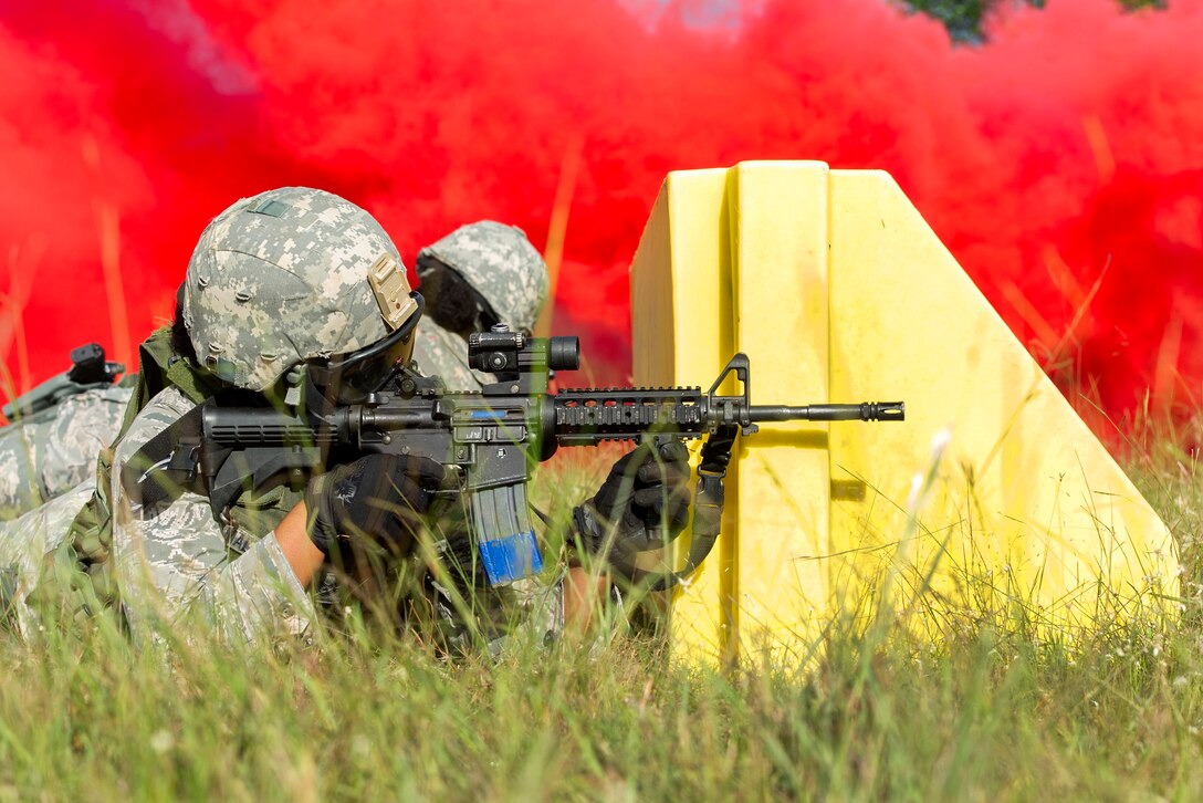 Airmen take cover from behind a block of concrete under the cover of red smoke and returns fire while participating in training to shoot, move and communicate.
