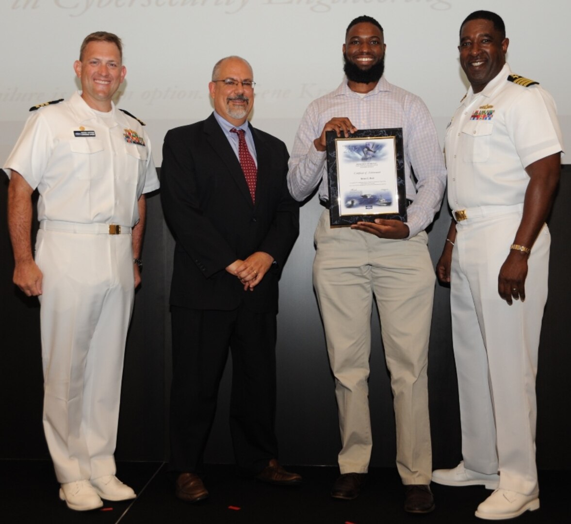 IMAGE: DAHLGREN, Va. - Brent Reid receives his certificate of achievement from Naval Surface Warfare Center Dahlgren Division (NSWCDD) Technical Director John Fiore, NSWCDD Commanding Officer Capt. Godfrey 'Gus' Weekes, right, and Combat Direction Systems Activity Dam Neck Commanding Officer Cmdr. Andrew Hoffman at the 2017 NSWCDD academic awards ceremony. Pasanen was recognized for completing his master's in cybersecurity engineering from Morgan State University, and commended for his commitment to personal and professional development.