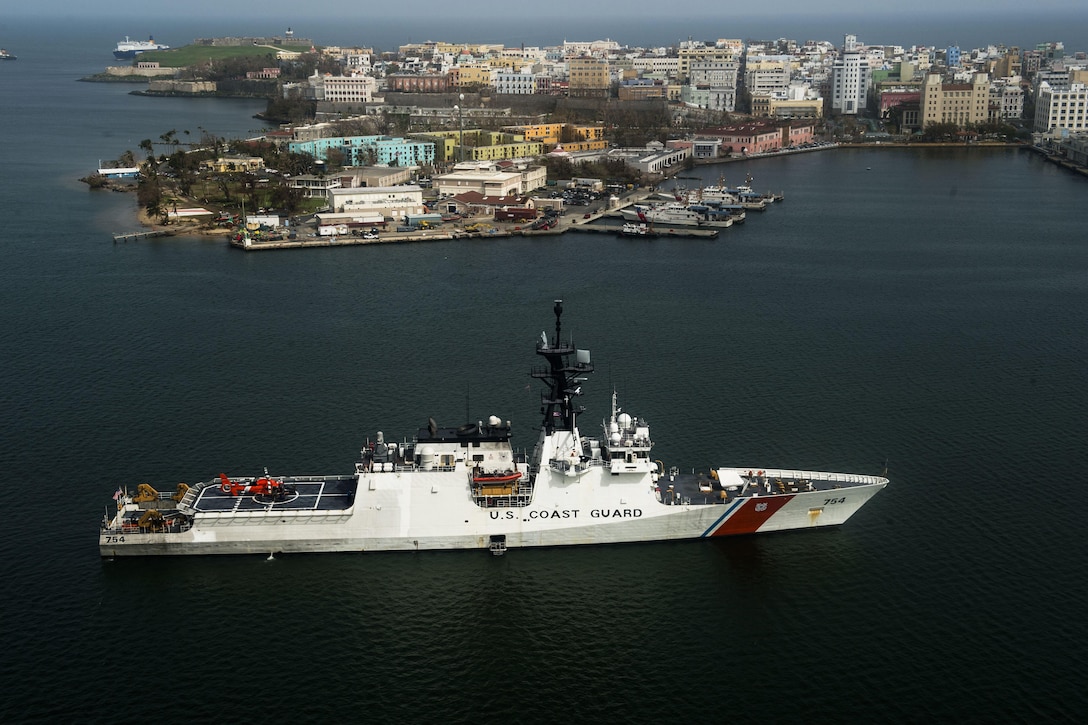 Seen from above, a Coast Guard ship sits in the water near shore.
