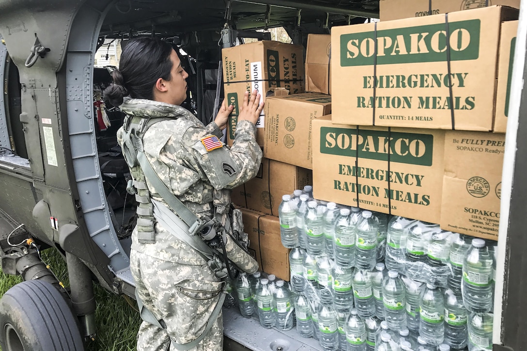 A soldier handles a cardboard box of emergency rations on a helicopter filled with provisions.