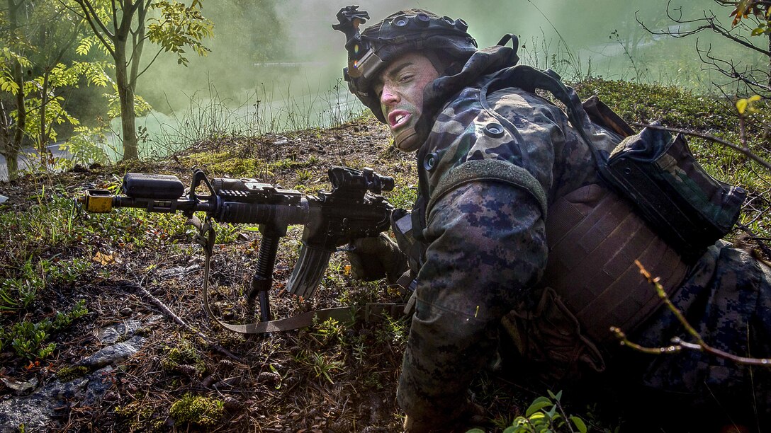 A Marine looks up while lying on the ground with a weapon.