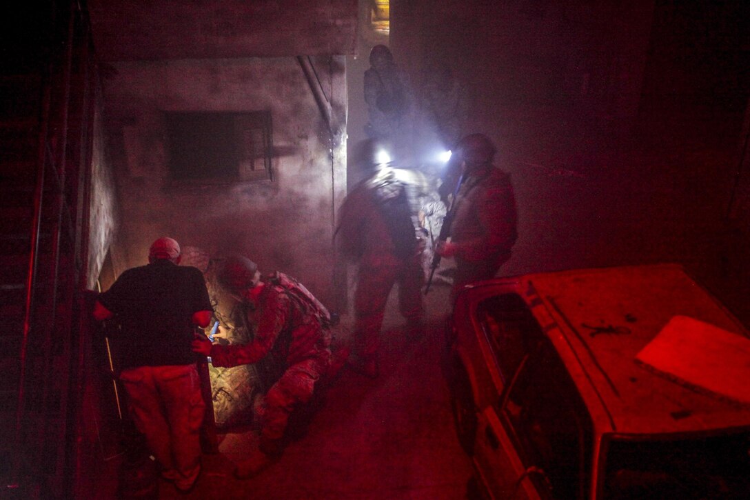 Airmen tend to someone on the floor in a dark room illuminated with red light.