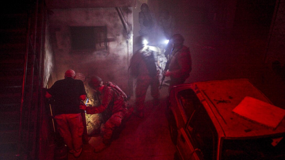 Airmen tend to someone on the floor in a dark room illuminated with red light.