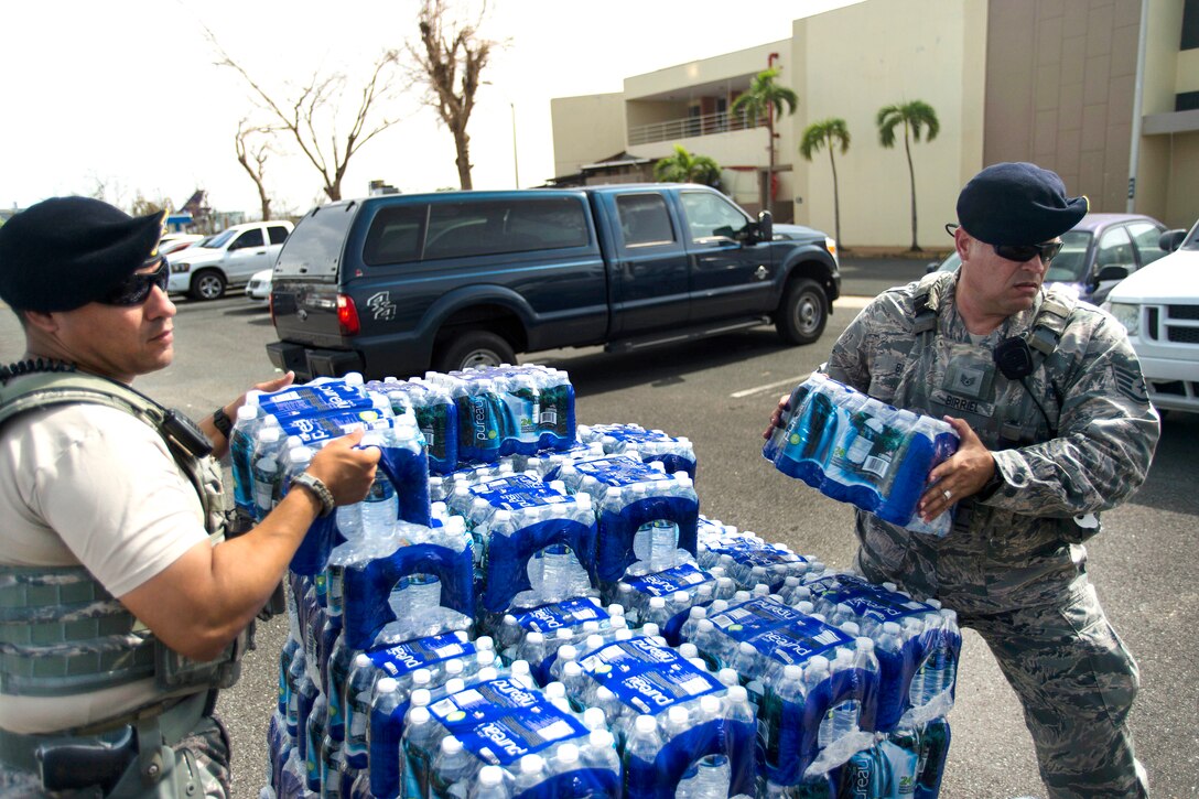 Two airmen lift cases of bottled water.