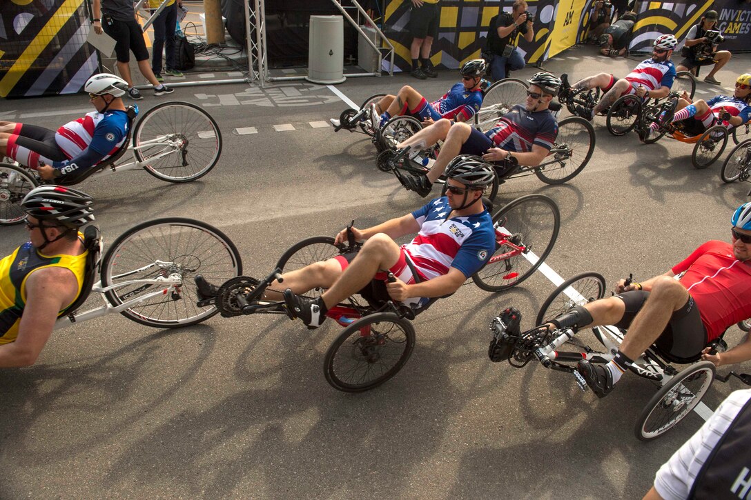 Recumbent cyclists ride past the start line on a road.