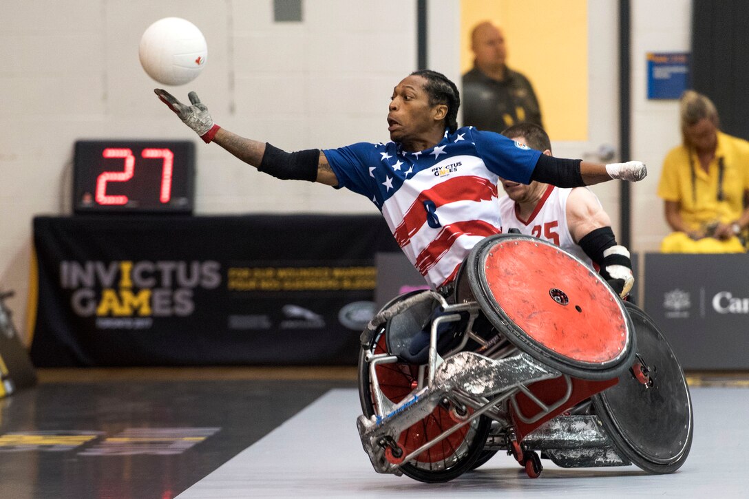 A person in a wheelchair with one wheel off the ground reaches for a ball.
