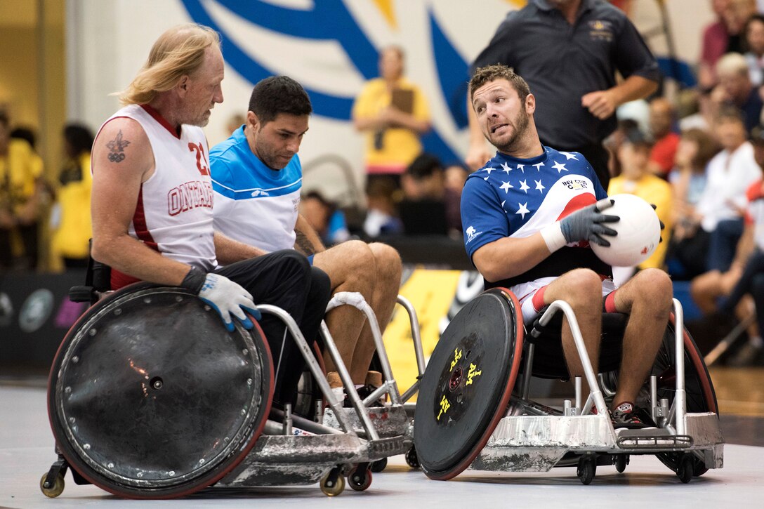 Two people in wheelchairs follow a person in a wheelchair with the ball.