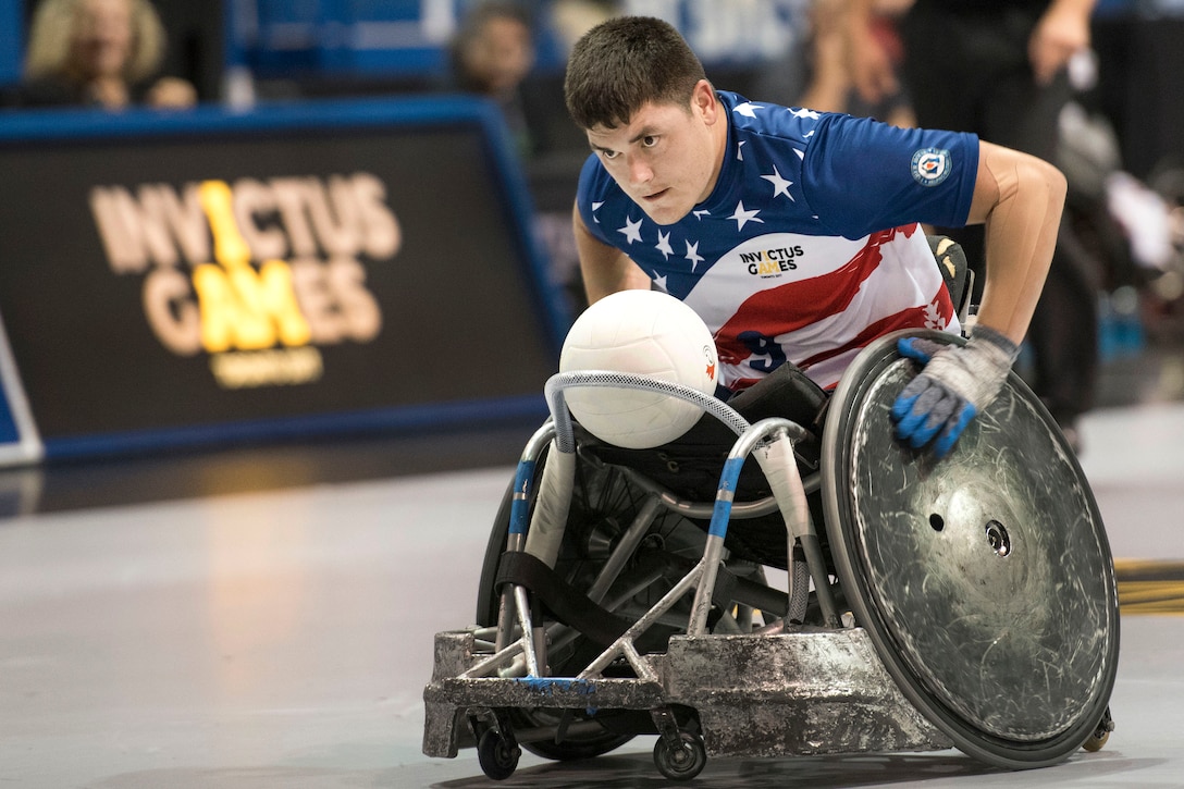 A person in a wheelchair moves down a court with a ball in his lap.