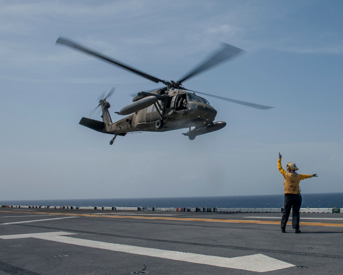 A Sailor signals the take off of a U.S. Army helicopter from the flight deck of the amphibious assault ship USS Wasp