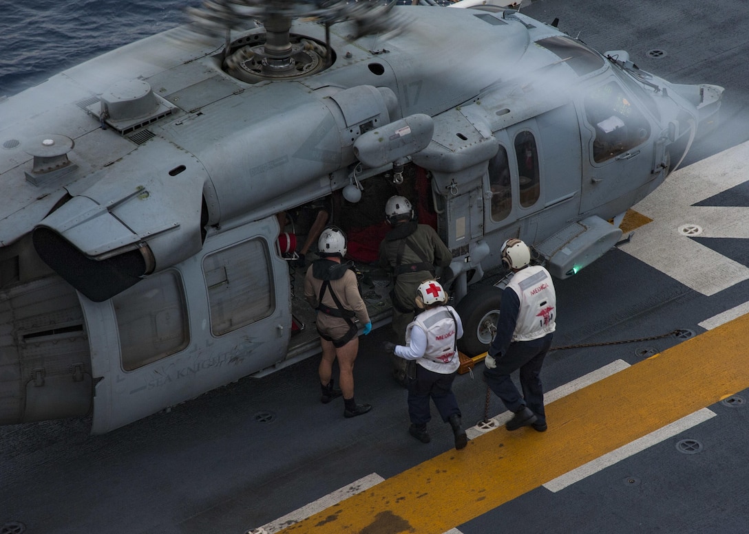 Sailors escort a rescued resident of French Guadalupe from a helicopter on the flight deck of USS Wasp.