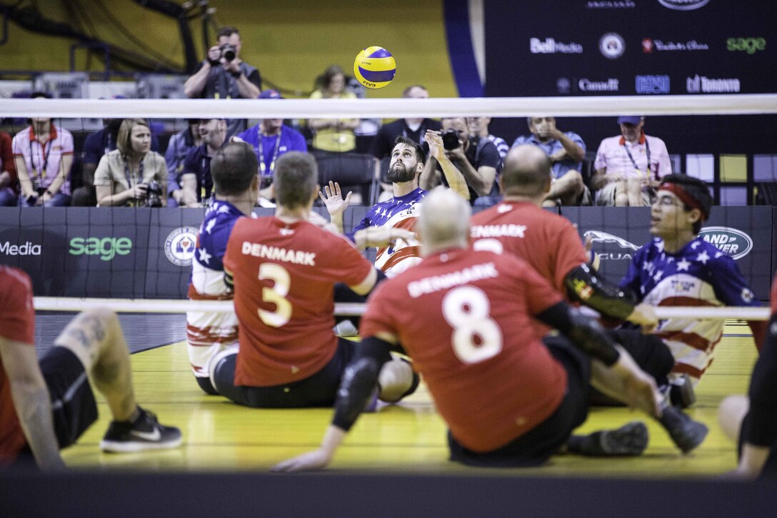 Two teams sit on the ground on each side of a volleyball net.