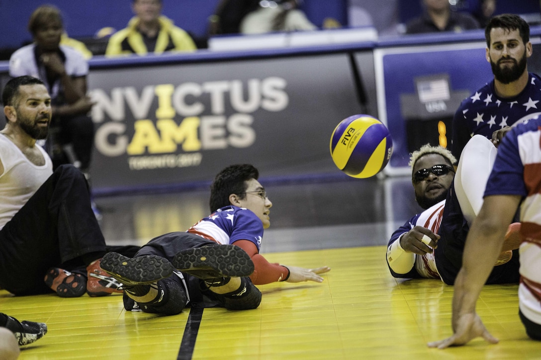 A player lays on the ground reaching for a volleyball.