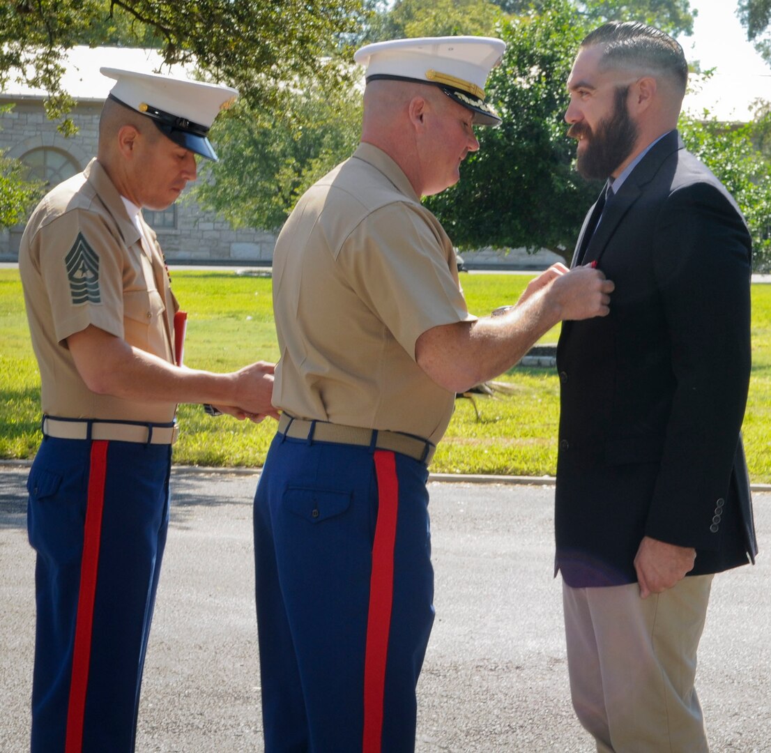 Lt. Col. William O'Brien (center), commanding officer, 3rd Assault Amphibian Battalion, Camp Pendleton, Calif., pins the Navy and Marine Corps Medal on Marine Corps veteran Corporal Randy D. Mann during a ceremony in the historical quadrangle at Joint Base San Antonio-Fort Sam Houston Sept. 8. Mann was awarded the medal during the ceremony in his hometown of San Antonio for his heroic actions while on active duty with the 3rdAssault Amphibian Battalion in July 2013.