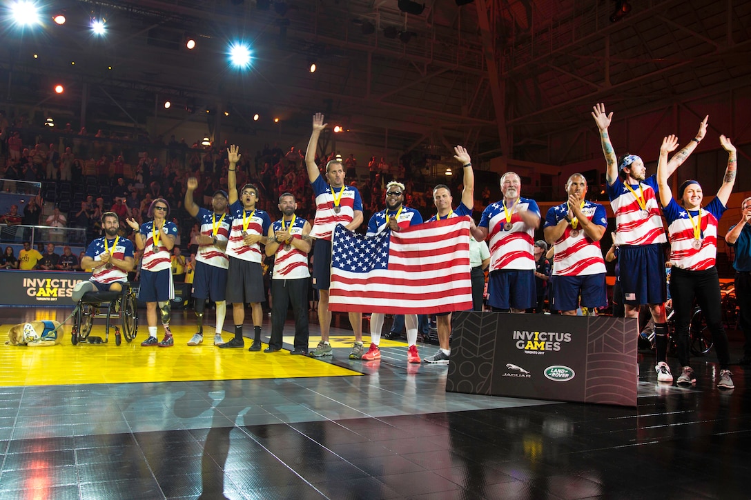 A line of athletes holding an American flag raise their hands.