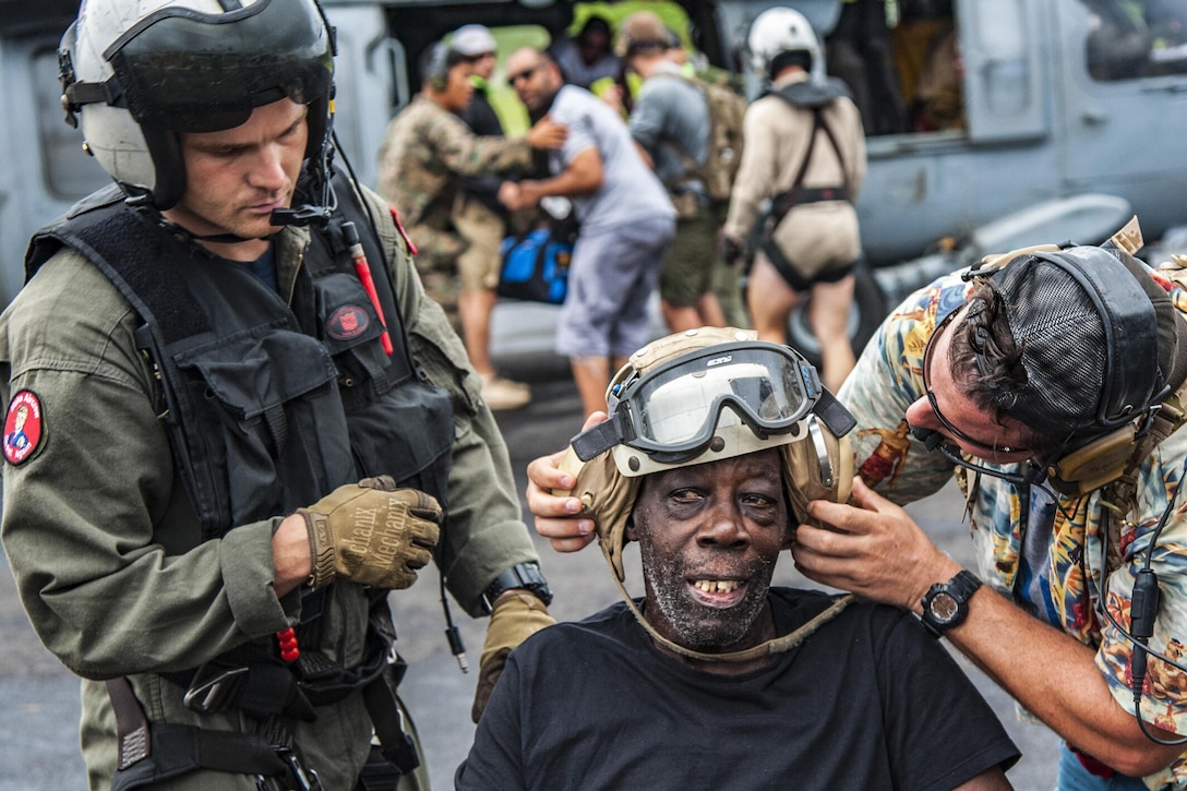 Two men work to put a helmet and goggles on a civilian.