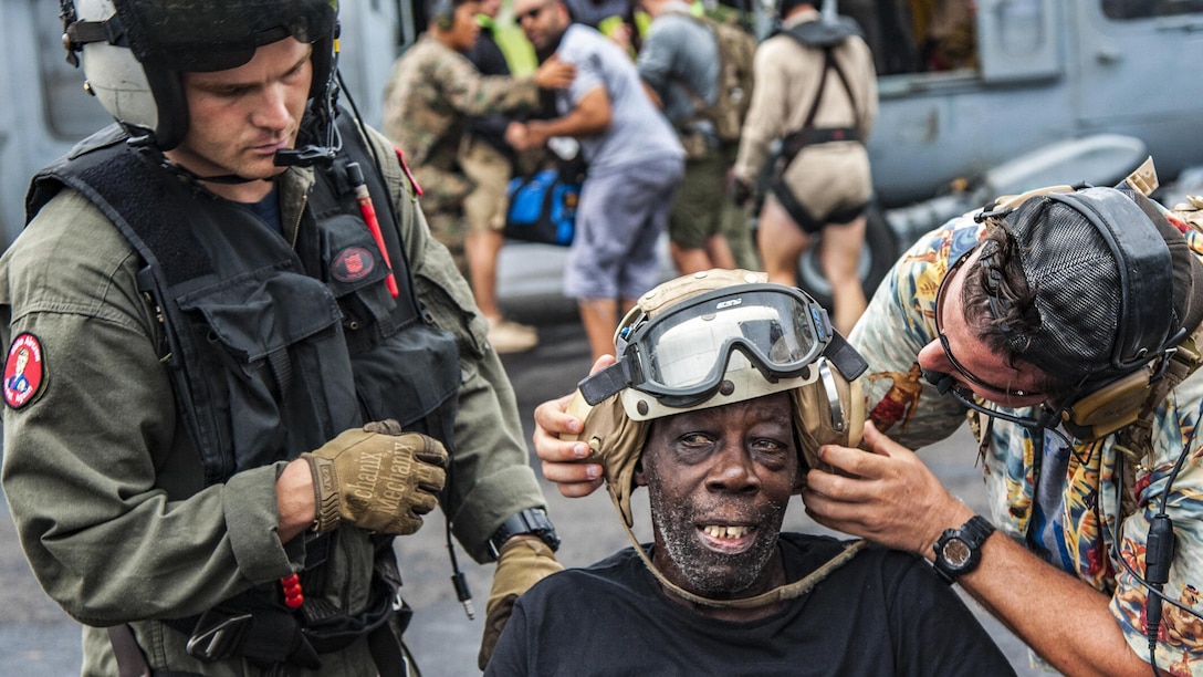 Two men work to put a helmet and goggles on a civilian.