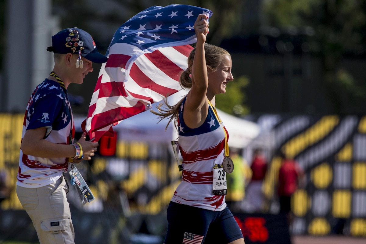A Marine veteran runs with a smile on her face, holding an American flag.