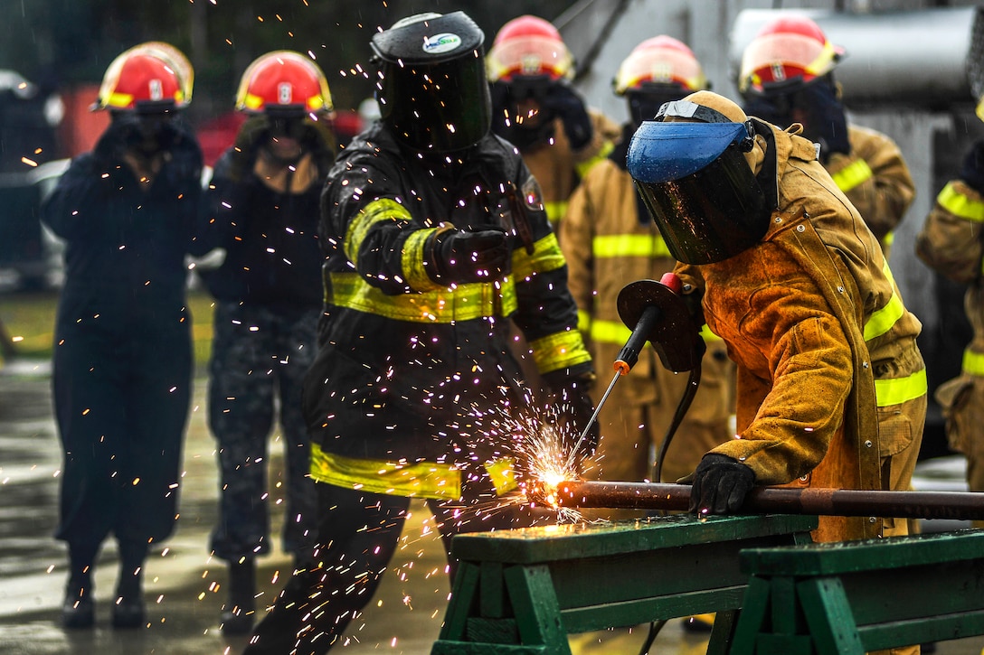 An instructor trains a sailor to use a cutting torch.