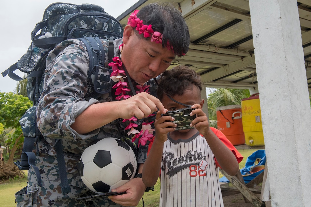 A Japanese service member shows a child his camera.