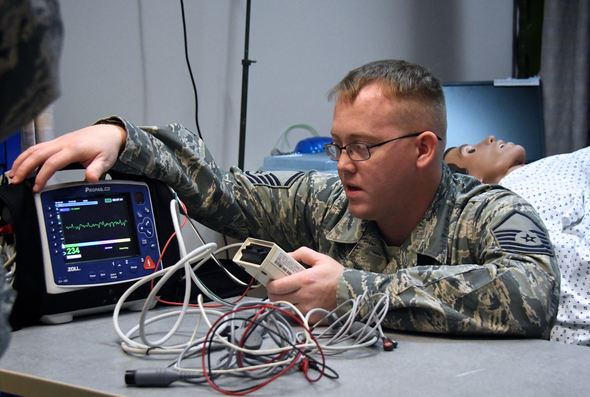 Master Sgt. Thomas Dissette, a member of the 932nd Airlift Wing's Medical Group, 932nd Aeromedical Staging Squadron, teaches a class on taking care of critically ill patients Mar. 6, 2018, at Scott Air Force Base, Ill.  He works through the steps required to use a piece of equipment called the "Propaq", which controls monitoring his simulated robotic patient, also known as "simulation man" (in background).  The Propaq MD offers multiple display modes to operate in bright sunlight or during night missions (NVG-friendly display). The battery system and AC power charger provide worldwide sea, land, and air operating capabilities for this device that Dissette used in the class. The system can monitor all physiologic parameters and provide numerous shocks for over six hours on a single battery charge.  (U.S. Air Force photo by Lt. Col. Stan Paregien)