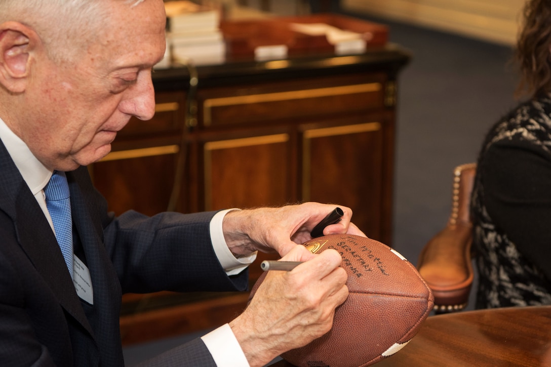 Defense Secretary James N. Mattis signs a football.