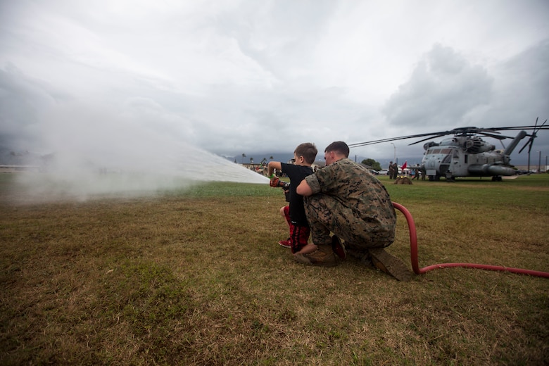 A U.S. Marine with Aircraft Rescue and Fire Fighting, Marine Corps Air Station Kaneohe Bay, helps a child spray a fire hose during ‘Operation Ooh-Rah Kids’, Marine Corps Base Hawaii (MCBH), March 23, 2018. MCBH Marines and Sailors volunteer each year to give the children a chance to experience what it’s like to be a Marine. (U.S. Marine Corps photo by Lance Cpl. Matthew Kirk)