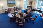 Defense Department leaders sit at a round table with a teenager.