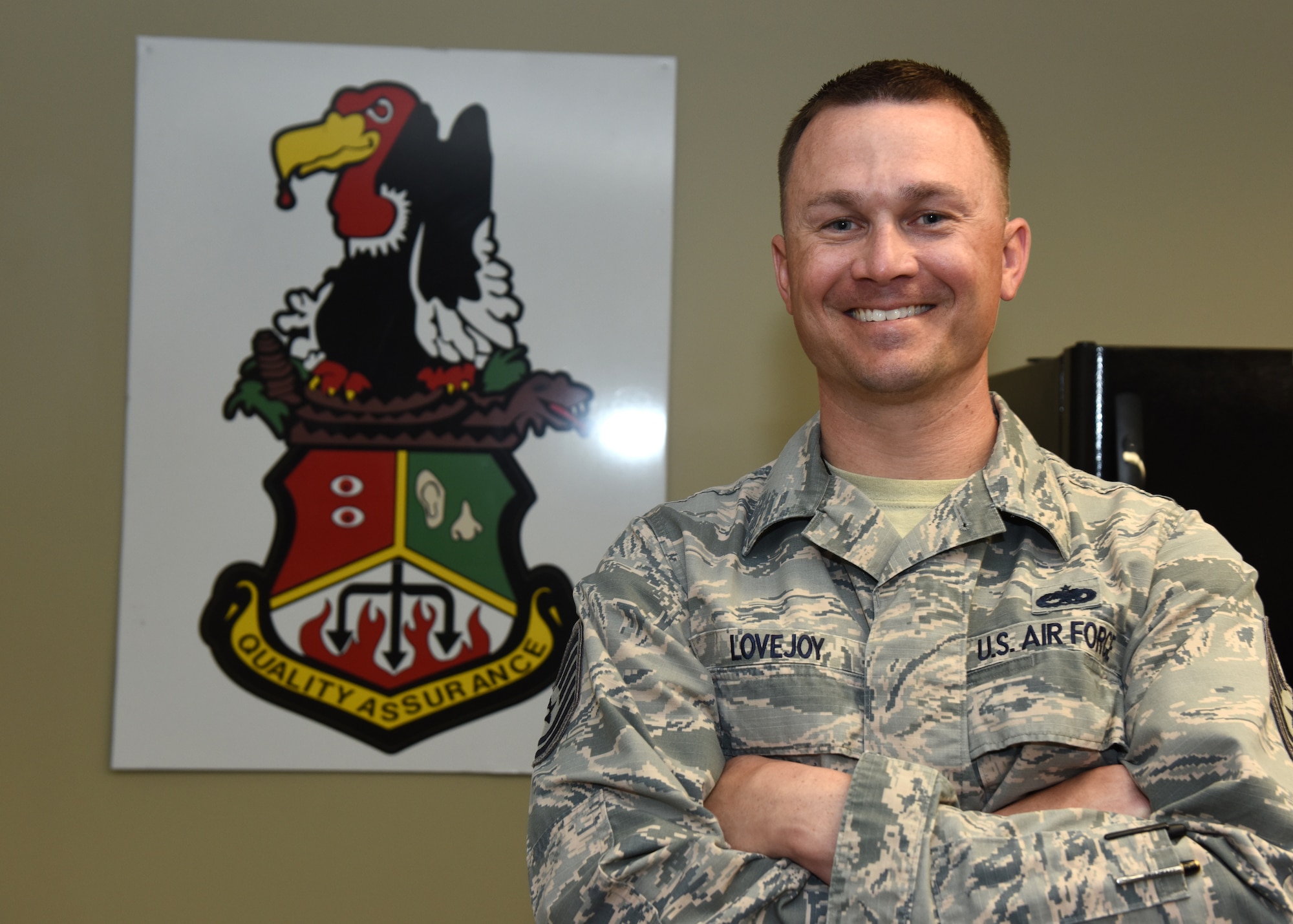 A in uniform male stands in front of a wall with picture of buzzard.