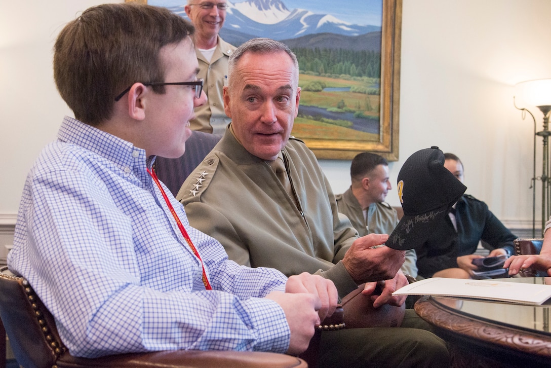Marine Corps Gen. Joe Dunford, chairman of the Joint Chiefs of Staff, hands a signed hat to a civilian.