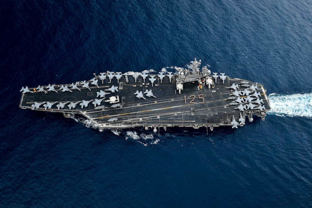Sailors, seen from overhead, form a "125" on a ship's flight deck as it travels.