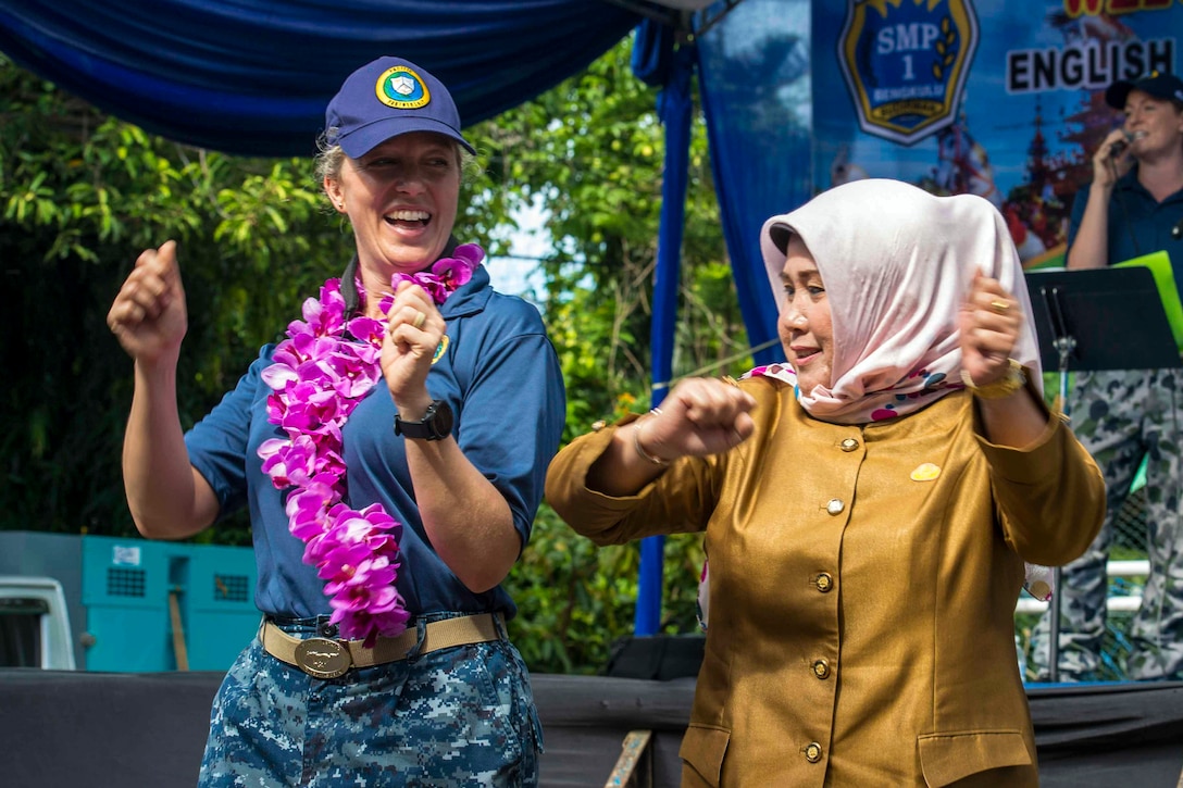 A sailor wearing a lei dances with a woman wearing a headscarf.
