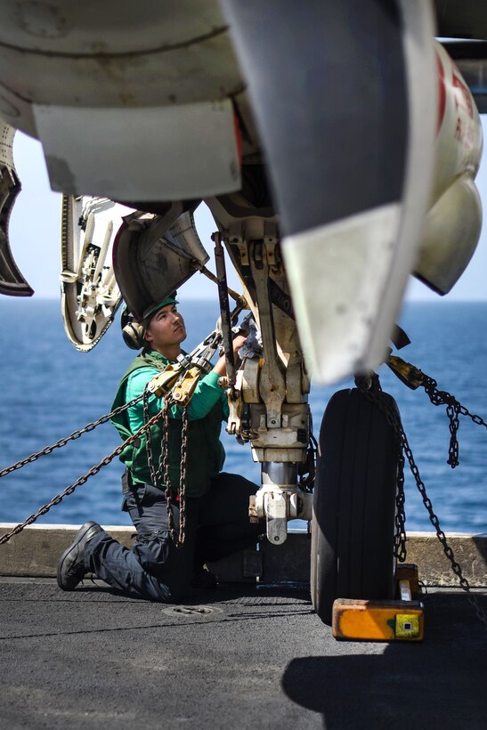 A sailor cleans the strut of a C-2A Greyhound aircraft.