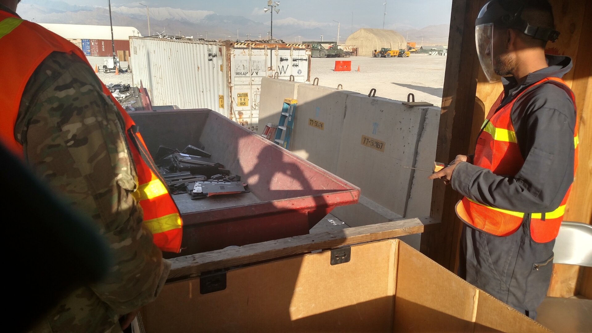 Property Disposal Specialist Antonio Acevedo (left), and a contractor employee use a trailer as a platform to safely load scrap material into a 7-foot shredder.