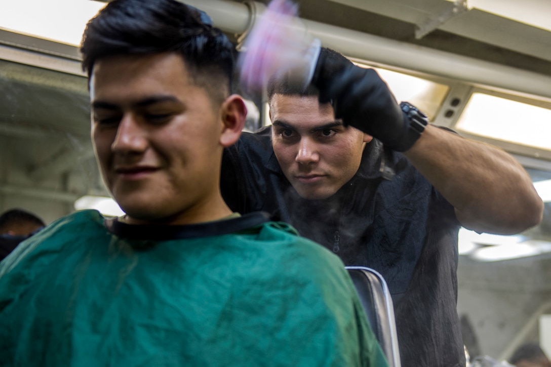 A Marine uses a pink brush to powder on the back of another Marine's head.
