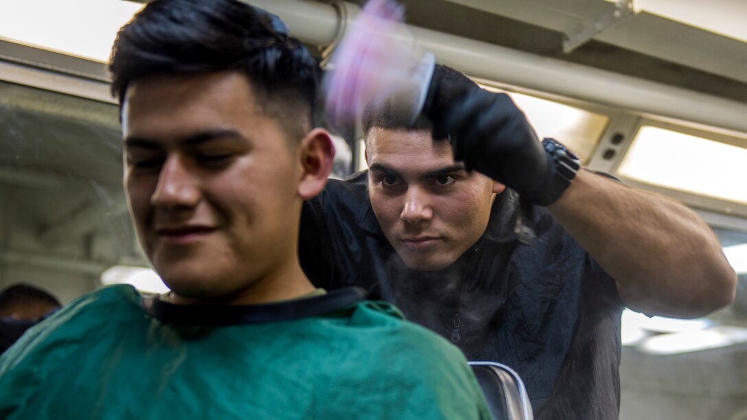A Marine uses a pink brush to powder on the back of another Marine's head.