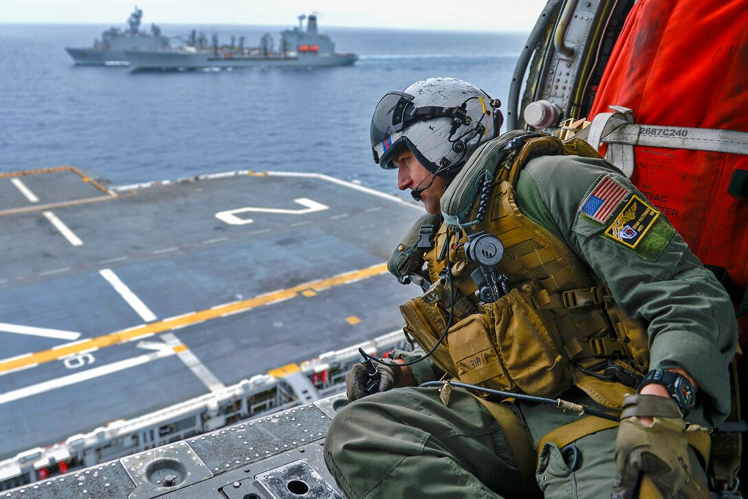 A sailor on a helicopter looks out over the flight deck of an assault ship.