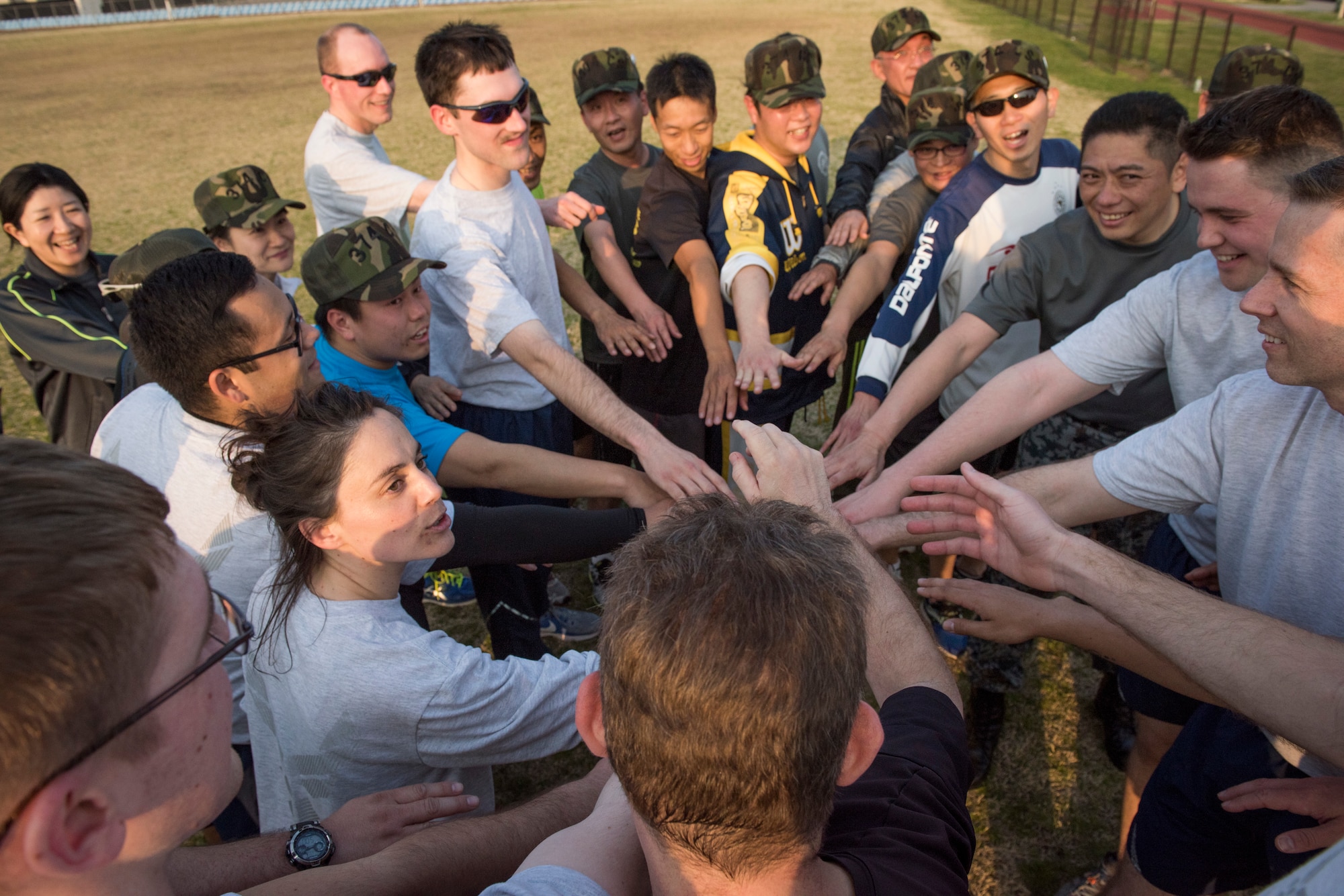 The U.S. Air Force 374th Communications Squadron and Japan Air Self-Defense Force Operational Support Wing members bring their hands in for a group cheer after a game of ultimate frisbee, March 28, 2018, at Yokota Air Base, Japan.